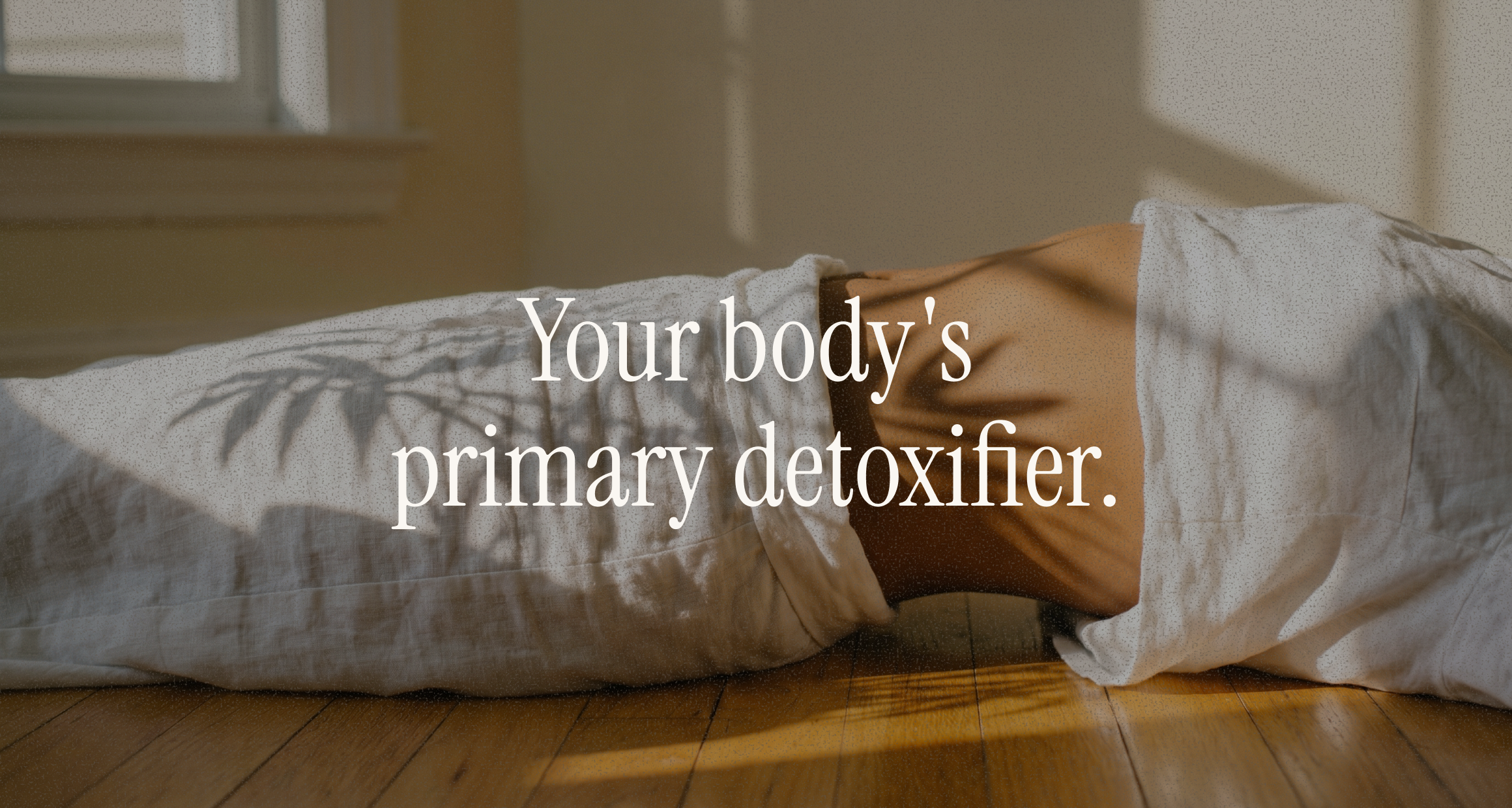 Person lying on a wood floor wrapped in linen in soft window light, overlay "Your body's primary detoxifier" — liver pillar.