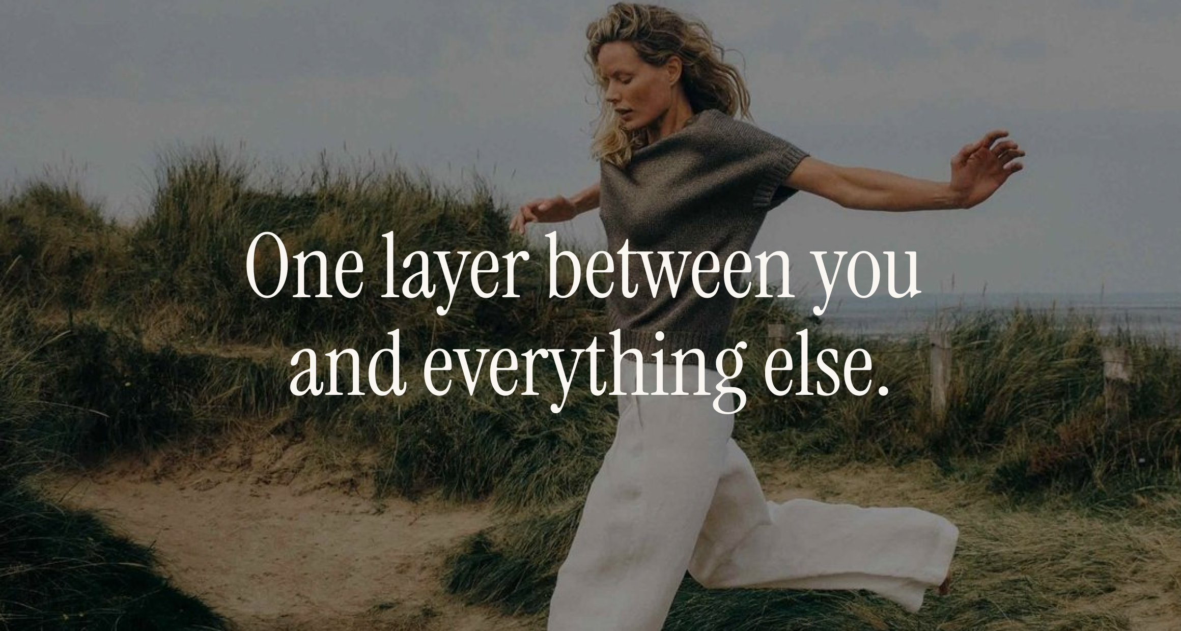 Woman running through grassy seaside dunes in soft daylight, overlay "One layer between you and everything else" — gut barrier pillar.